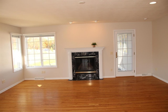 unfurnished living room with light wood-style flooring, a premium fireplace, visible vents, and baseboards