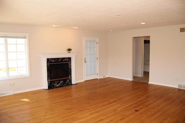 unfurnished living room with light wood finished floors, a high end fireplace, visible vents, and baseboards