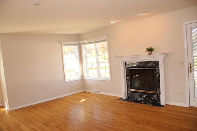 unfurnished living room with wood finished floors, a high end fireplace, and visible vents