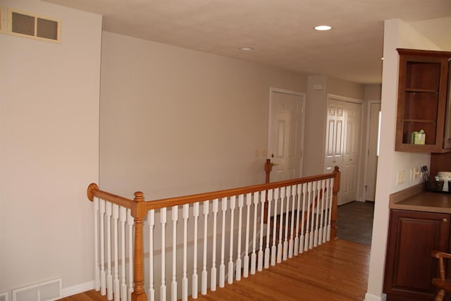 hallway featuring an upstairs landing, visible vents, wood finished floors, and recessed lighting