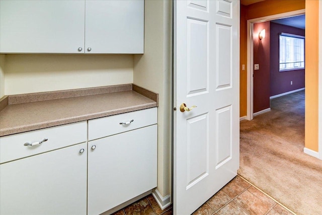 kitchen with baseboards, light tile patterned floors, white cabinetry, and light colored carpet