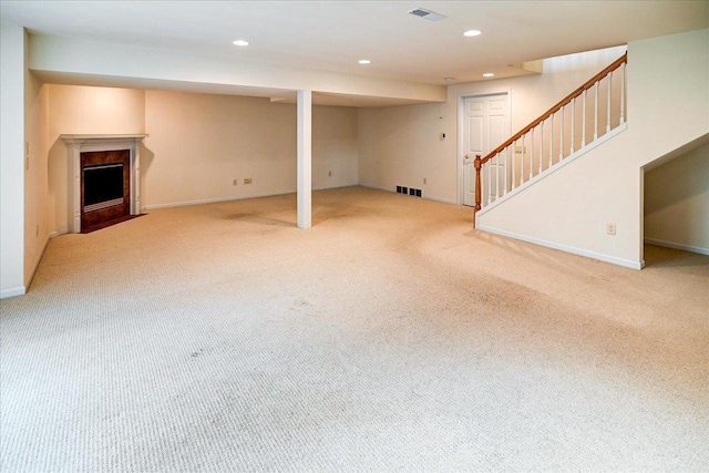 finished below grade area with recessed lighting, a fireplace with flush hearth, visible vents, and light colored carpet