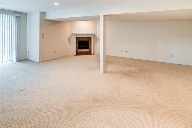 unfurnished living room featuring baseboards, a fireplace with flush hearth, and light colored carpet