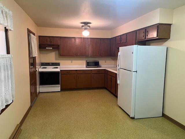 kitchen with light countertops, dark brown cabinetry, white appliances, under cabinet range hood, and baseboards