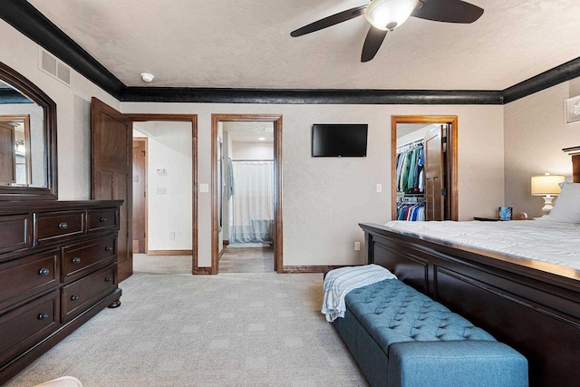 bedroom featuring light carpet, baseboards, visible vents, a walk in closet, and crown molding