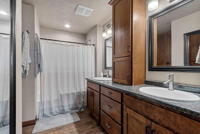 bathroom with double vanity, a textured ceiling, a sink, and wood finished floors