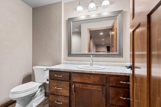 half bath featuring a textured wall, vanity, and toilet