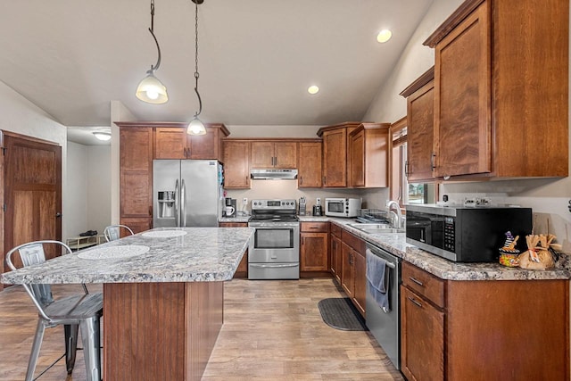 kitchen with brown cabinetry, a breakfast bar area, stainless steel appliances, under cabinet range hood, and a sink