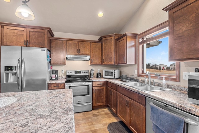 kitchen featuring under cabinet range hood, a sink, light wood-style floors, hanging light fixtures, and appliances with stainless steel finishes