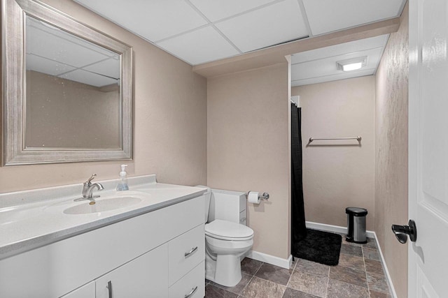 full bath featuring baseboards, a drop ceiling, toilet, stone finish flooring, and vanity