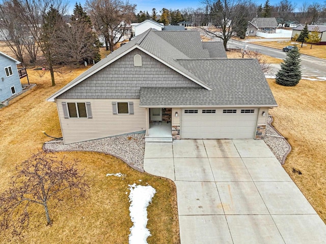 view of front facade with a shingled roof, concrete driveway, an attached garage, a front yard, and stone siding