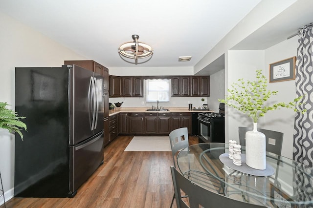 kitchen featuring range with gas cooktop, dark brown cabinetry, freestanding refrigerator, dark wood-style floors, and a sink