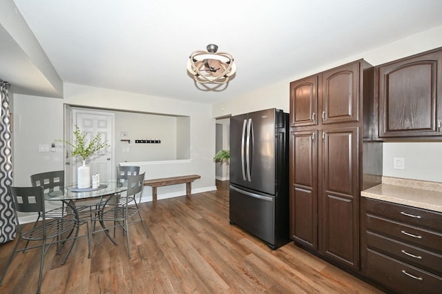 kitchen featuring wood finished floors, baseboards, freestanding refrigerator, light countertops, and dark brown cabinetry