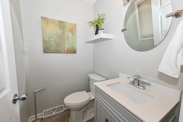 half bathroom with visible vents, toilet, vanity, and wood finished floors