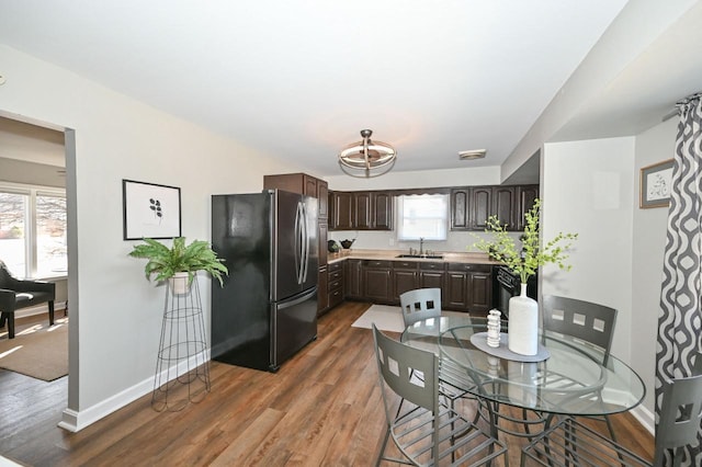 kitchen featuring dark wood-style floors, baseboards, freestanding refrigerator, a sink, and dark brown cabinetry