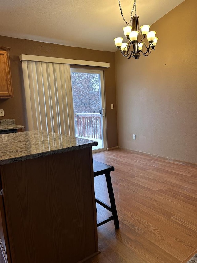 kitchen featuring dark stone countertops, a notable chandelier, hanging light fixtures, and light wood finished floors