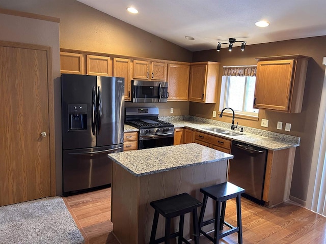 kitchen featuring a center island, light wood finished floors, lofted ceiling, appliances with stainless steel finishes, and a sink