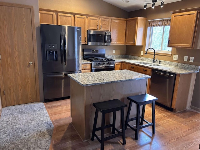 kitchen featuring lofted ceiling, appliances with stainless steel finishes, a sink, a kitchen island, and light wood-type flooring