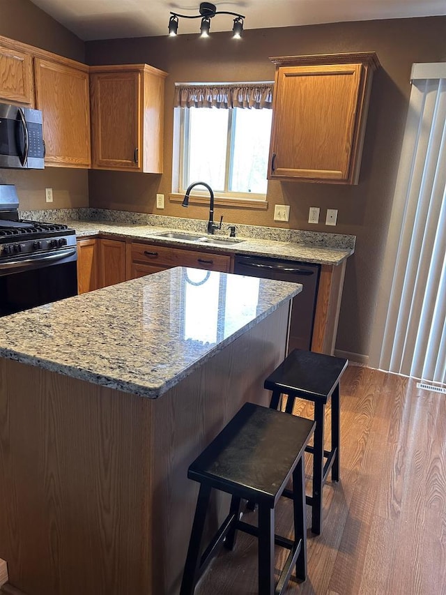 kitchen with dishwasher, a breakfast bar area, stainless steel microwave, wood finished floors, and a sink