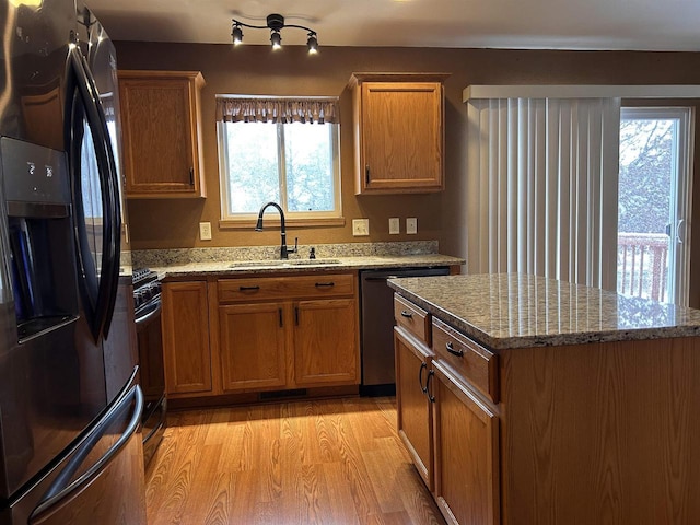 kitchen with light stone countertops, a sink, light wood-style floors, brown cabinets, and black appliances