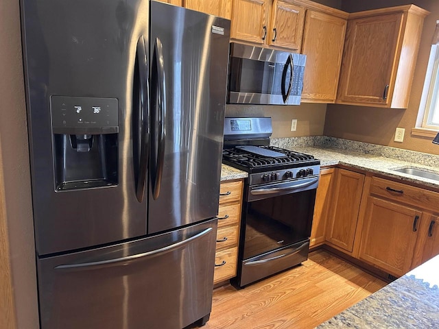 kitchen with brown cabinets, light stone countertops, stainless steel appliances, light wood-type flooring, and a sink