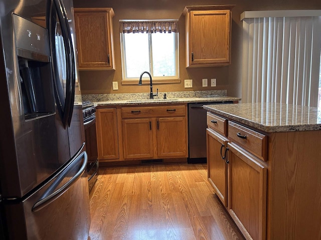 kitchen featuring range with gas cooktop, brown cabinets, black fridge, light wood-type flooring, and a sink