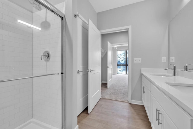 bathroom with double vanity, a stall shower, baseboards, wood finished floors, and a sink