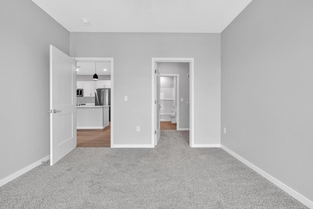 unfurnished bedroom featuring baseboards, carpet flooring, and freestanding refrigerator