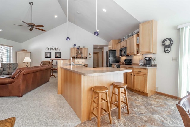 kitchen featuring light countertops, open floor plan, light brown cabinets, black appliances, and a kitchen bar