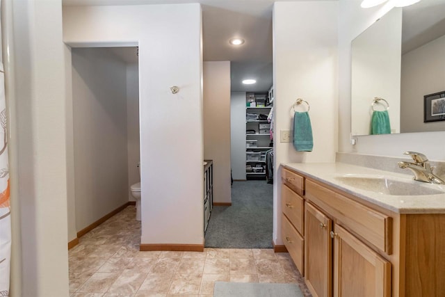 bathroom with toilet, baseboards, a walk in closet, and vanity