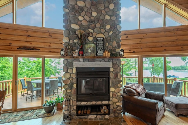 living area featuring a stone fireplace, a high ceiling, wood-type flooring, and a wealth of natural light