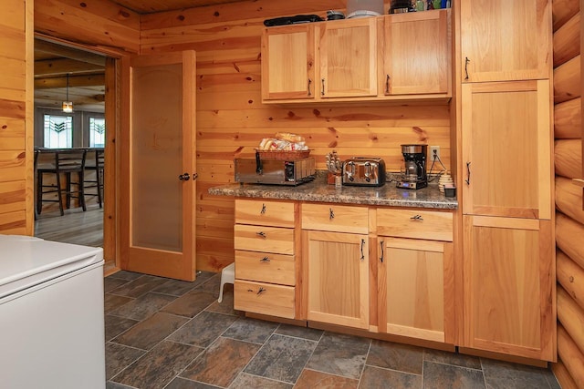 kitchen with light brown cabinetry, stone finish flooring, and wooden walls