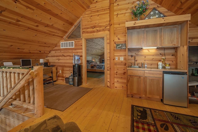 kitchen featuring wooden walls, refrigerator, visible vents, light wood-style floors, and vaulted ceiling