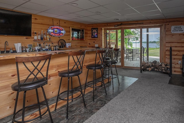 bar with indoor wet bar, a sink, a paneled ceiling, and wooden walls