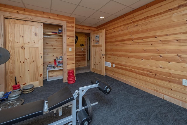 workout room featuring a drop ceiling, dark carpet, visible vents, and wooden walls