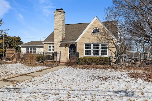 tudor-style house featuring stone siding, a chimney, fence, and roof with shingles