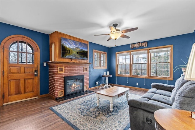 living area featuring a ceiling fan, a fireplace, baseboards, and wood finished floors