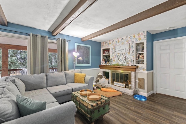 living room with a textured ceiling, wood finished floors, wainscoting, a brick fireplace, and beamed ceiling