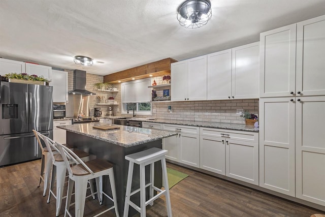 kitchen with wall chimney exhaust hood, open shelves, dark wood-type flooring, stainless steel fridge, and a kitchen bar