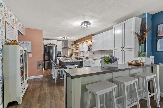kitchen featuring a breakfast bar, dark wood-style flooring, white cabinetry, wall chimney range hood, and stainless steel fridge