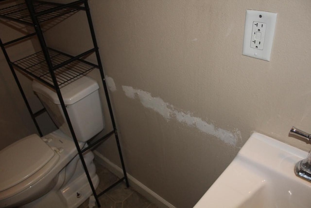 half bathroom featuring baseboards, a textured wall, and toilet