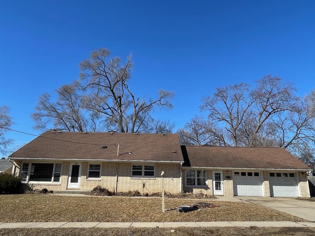 single story home with concrete driveway, brick siding, roof with shingles, and an attached garage