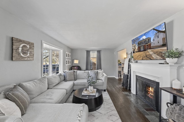 living area with dark wood-type flooring, a fireplace with flush hearth, and baseboards