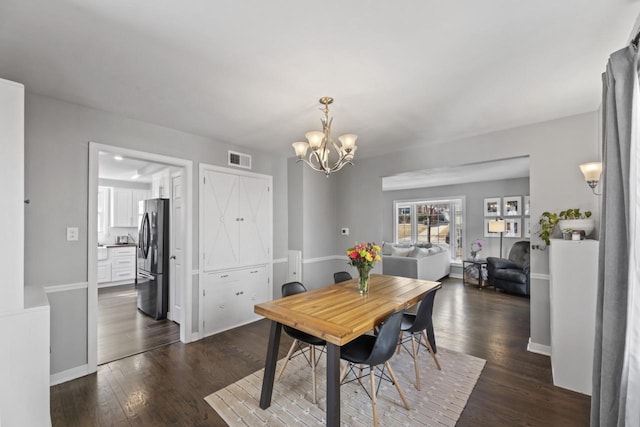 dining area with dark wood finished floors, baseboards, visible vents, and a chandelier