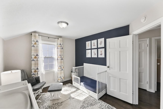 bedroom featuring baseboards, dark wood-type flooring, a nursery area, and vaulted ceiling