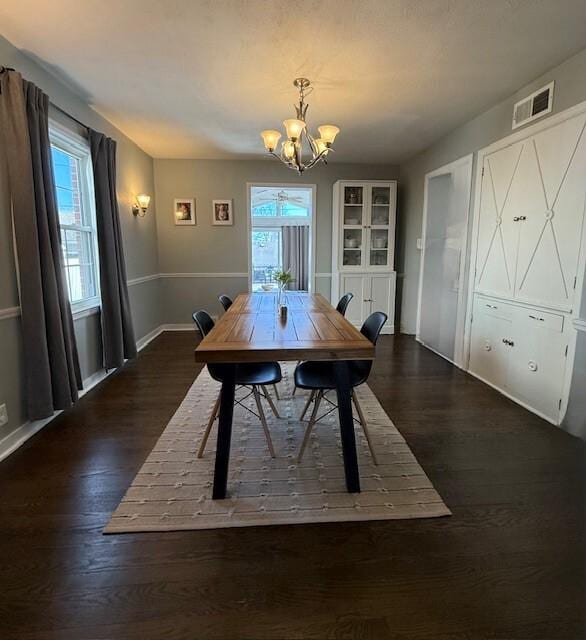 dining area featuring dark wood-style floors, visible vents, a healthy amount of sunlight, and a notable chandelier