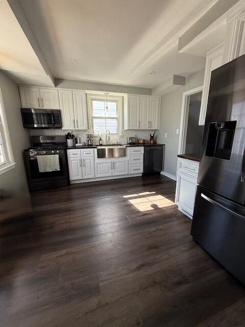 kitchen featuring dark wood finished floors, a sink, stainless steel appliances, white cabinets, and dark countertops