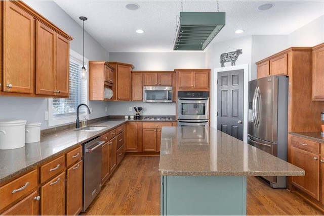 kitchen with appliances with stainless steel finishes, a kitchen island, a sink, and brown cabinets