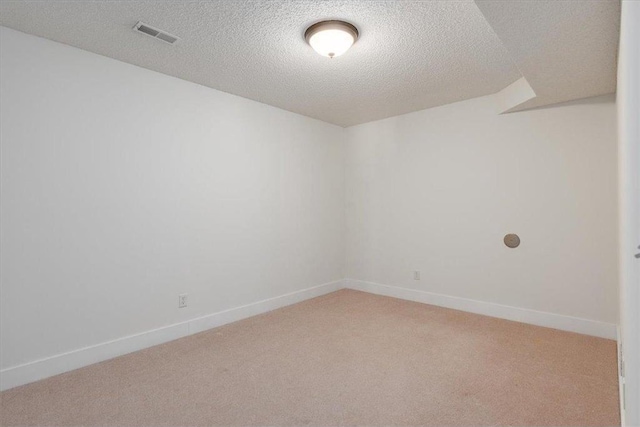 spare room with baseboards, visible vents, a textured ceiling, and light colored carpet