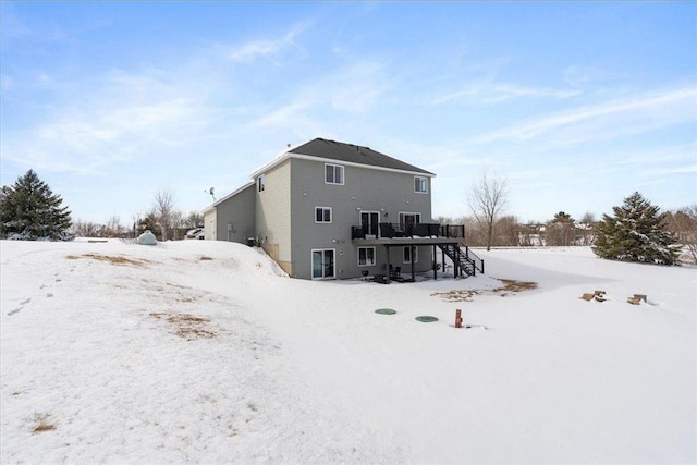 snow covered house with stairway and a wooden deck